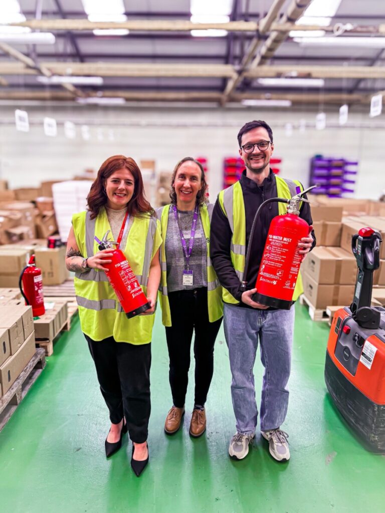 carrianne, mel and alex stood at safelincs hq with some of their fire extinguisher products